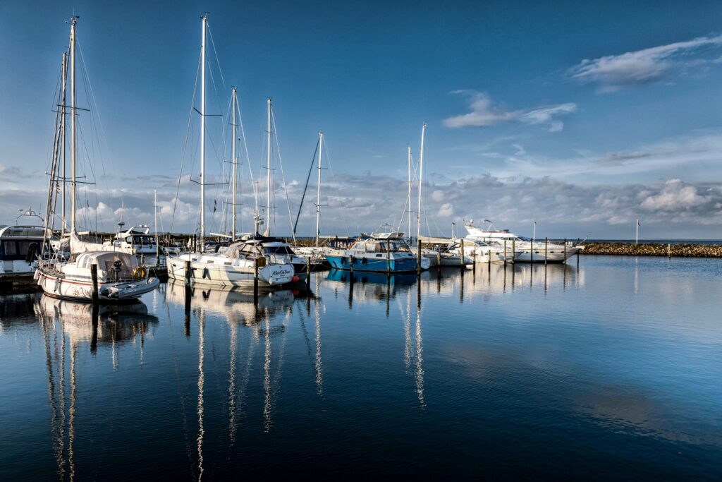 A tranquil view of sailboats in Årøsund harbor with calm waters reflecting a summer sky.